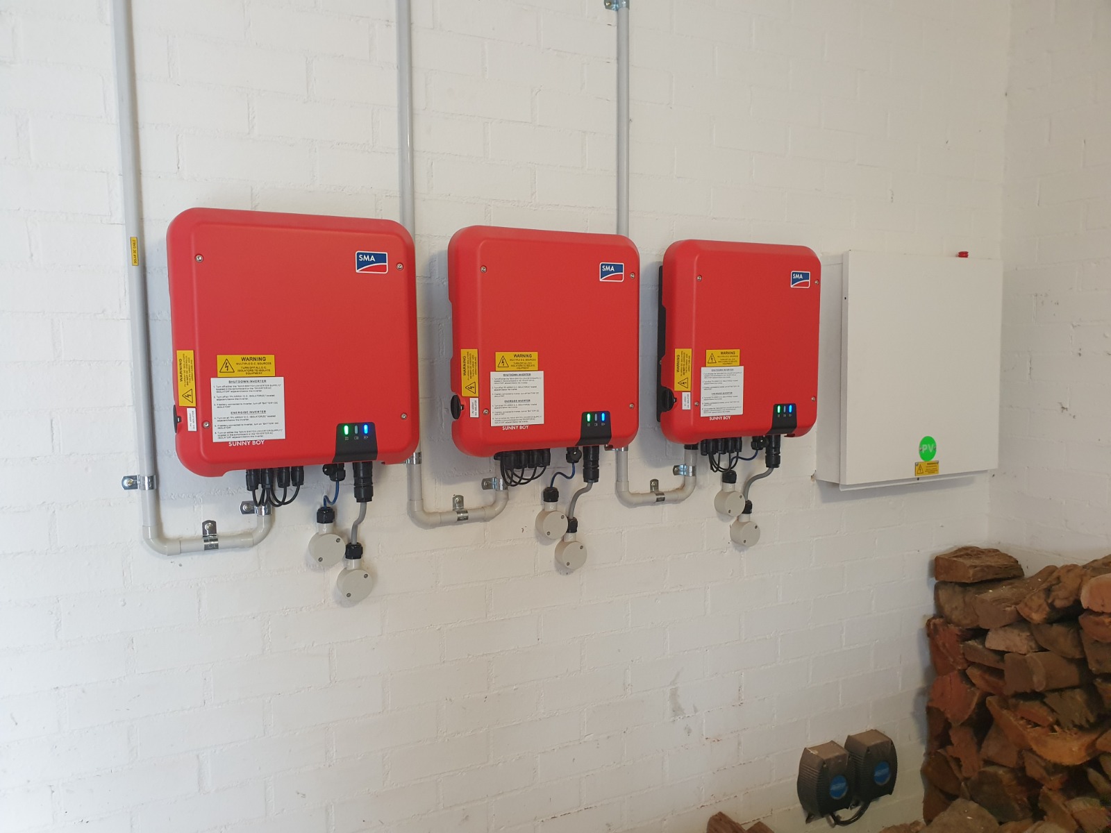 Three red SMA solar inverters mounted on a brick wall